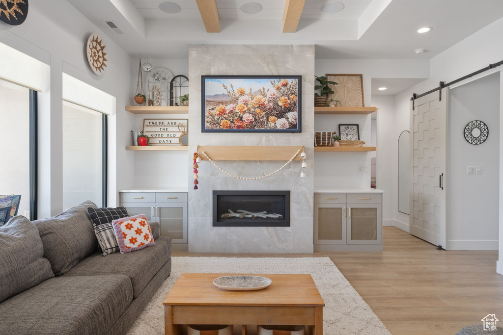 Living area featuring a barn door, beam ceiling, light wood finished floors, recessed lighting, and a high end fireplace