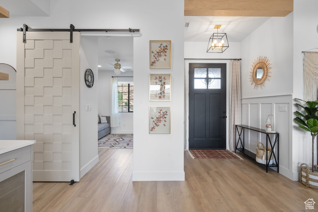 Foyer featuring wainscoting, a barn door, light wood finished floors, and ceiling fan with notable chandelier