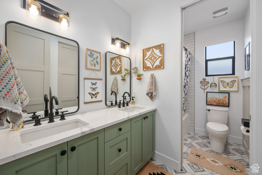 Full bathroom with baseboards, double vanity, toilet, and a sink