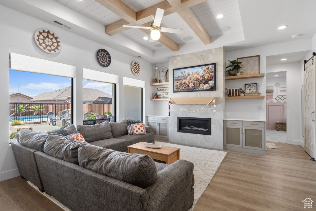 Living area featuring visible vents, a barn door, beam ceiling, light wood-style flooring, and a premium fireplace