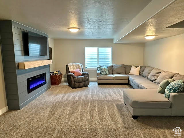 Living area featuring a glass covered fireplace, carpet floors, baseboards, and a textured ceiling