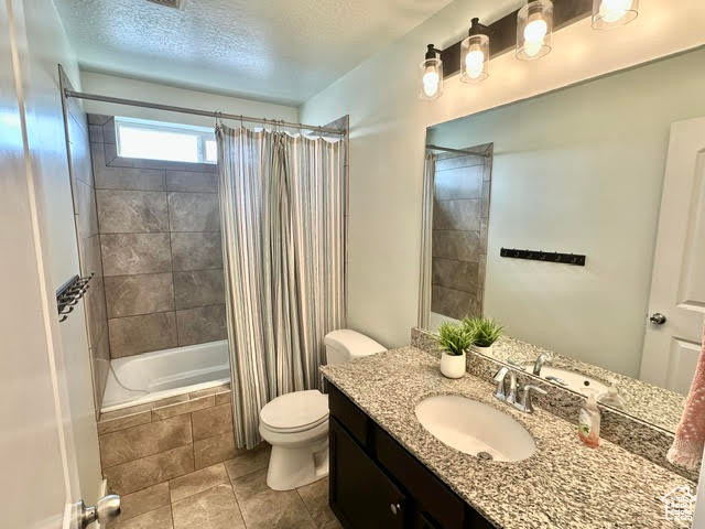 Full bathroom featuring a textured ceiling, tile patterned flooring, vanity, tiled shower / bath, and toilet