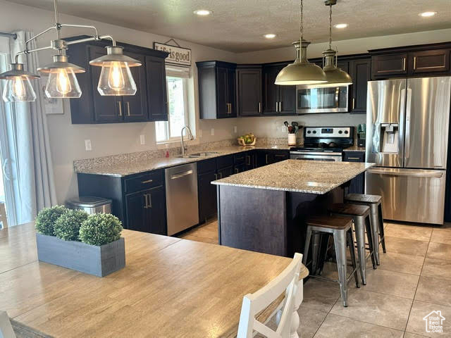 Kitchen featuring light stone counters, appliances with stainless steel finishes, a sink, a center island, and decorative light fixtures