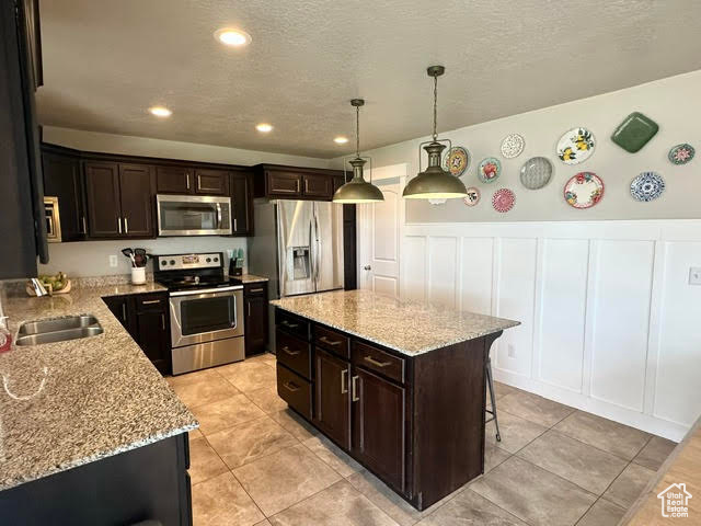 Kitchen featuring a kitchen bar, stainless steel appliances, light stone countertops, a sink, and a decorative wall
