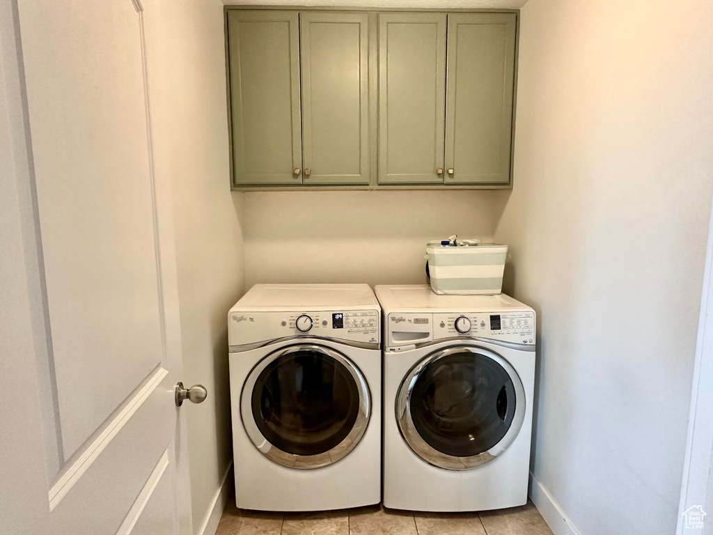 Clothes washing area featuring light tile patterned floors, baseboards, cabinet space, and washer and dryer