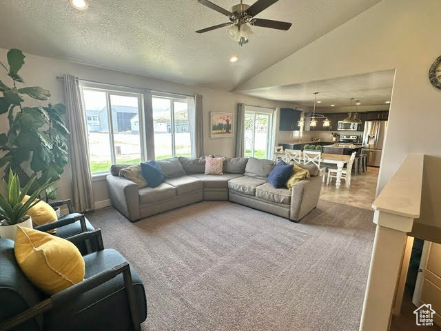 Living room with ceiling fan, light colored carpet, a textured ceiling, and lofted ceiling