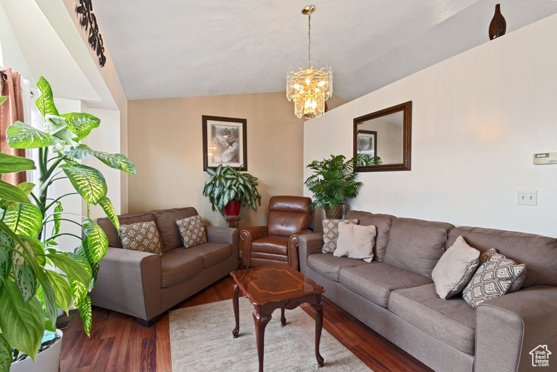 Living room with vaulted ceiling, wood finished floors, and a notable chandelier