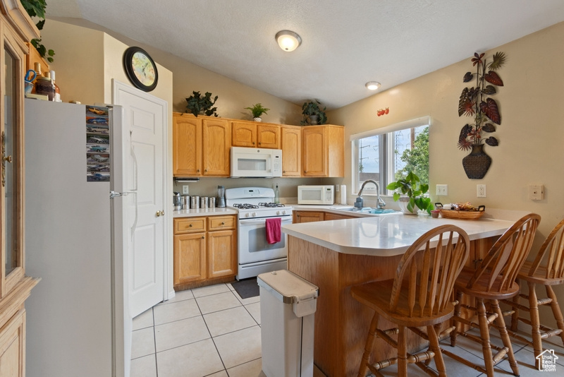 Kitchen featuring a breakfast bar area, a sink, light countertops, a peninsula, and white appliances