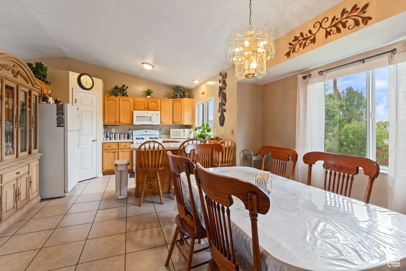 Dining room featuring light tile patterned floors, vaulted ceiling, and a notable chandelier