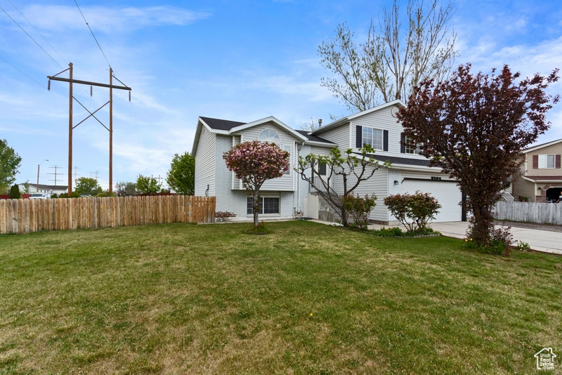 Exterior space featuring fence, an attached garage, concrete driveway, and a front yard