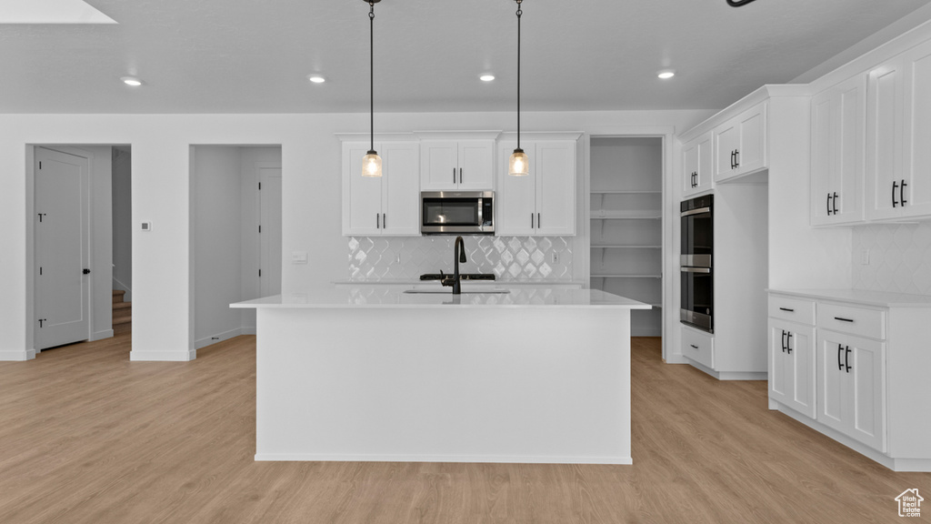 Kitchen featuring decorative backsplash, light wood-style floors, light countertops, a sink, and appliances with stainless steel finishes
