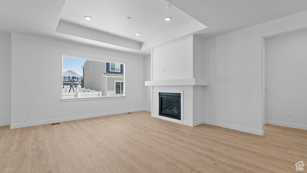 Unfurnished living room featuring recessed lighting, light wood-style flooring, a raised ceiling, and a fireplace