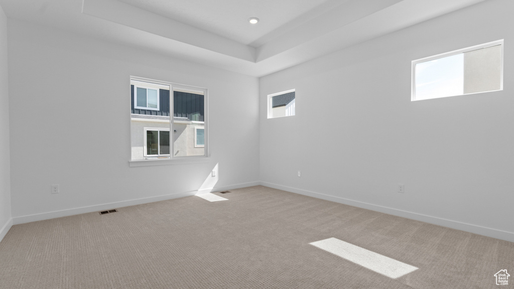 Carpeted empty room with baseboards, visible vents, and a raised ceiling