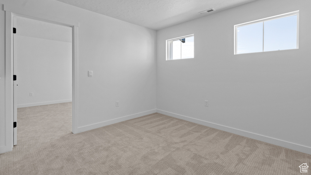 Empty room with light colored carpet, baseboards, visible vents, and a textured ceiling