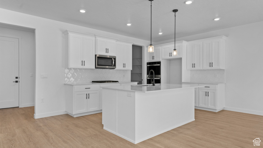 Kitchen featuring light countertops, black stovetop, stainless steel microwave, a sink, and light wood-style flooring