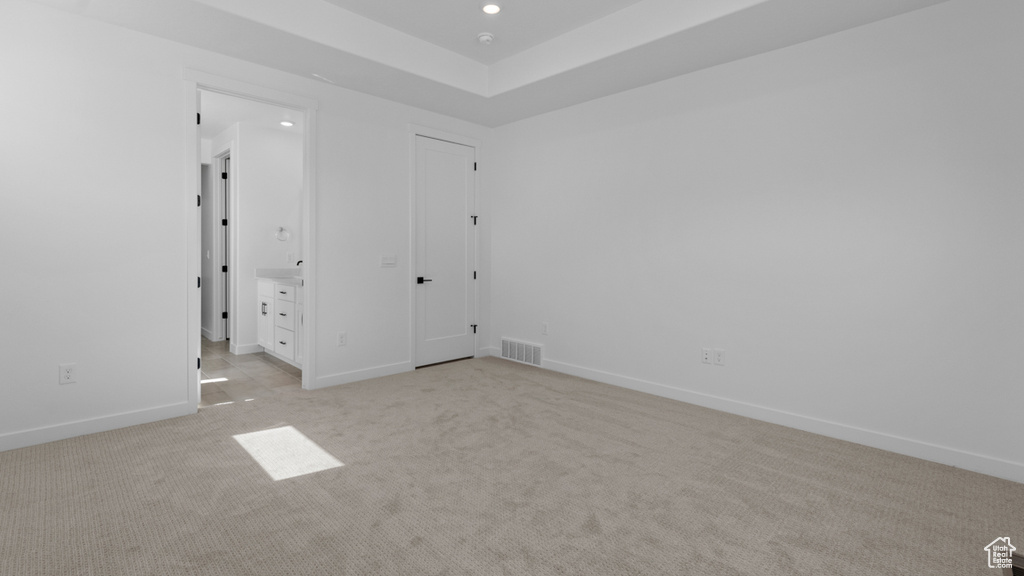 Unfurnished bedroom featuring visible vents, light carpet, baseboards, recessed lighting, and a tray ceiling