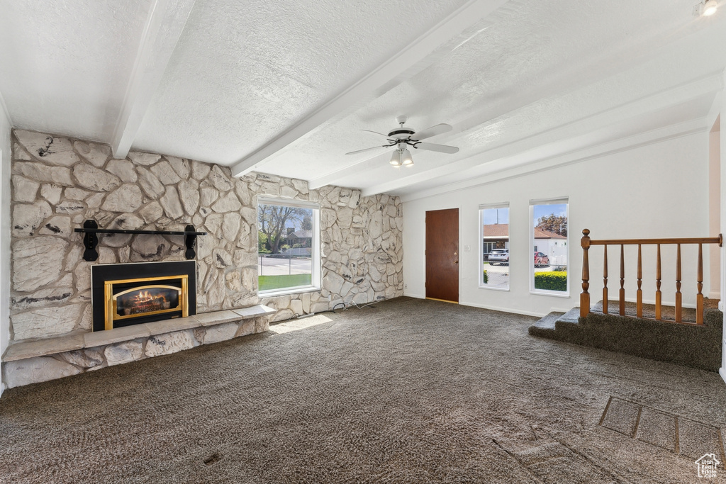 Unfurnished living room featuring ceiling fan, a textured ceiling, a fireplace, beamed ceiling, and carpet flooring