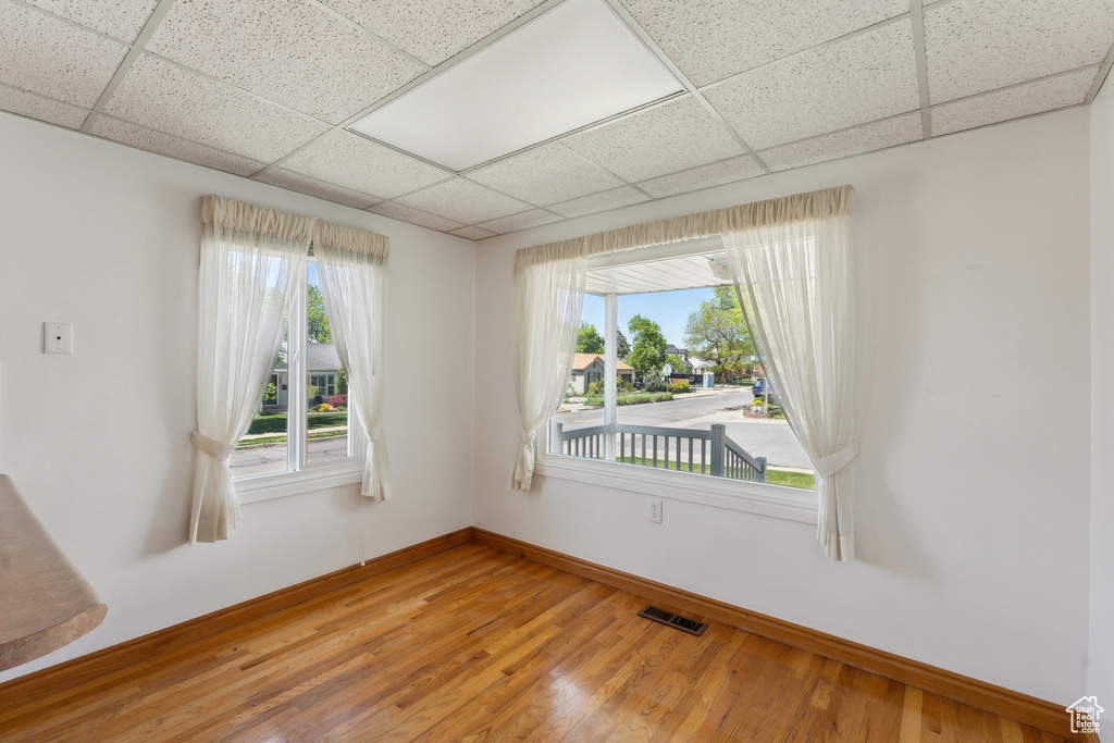 Empty room featuring baseboards, visible vents, light wood-type flooring, and a paneled ceiling