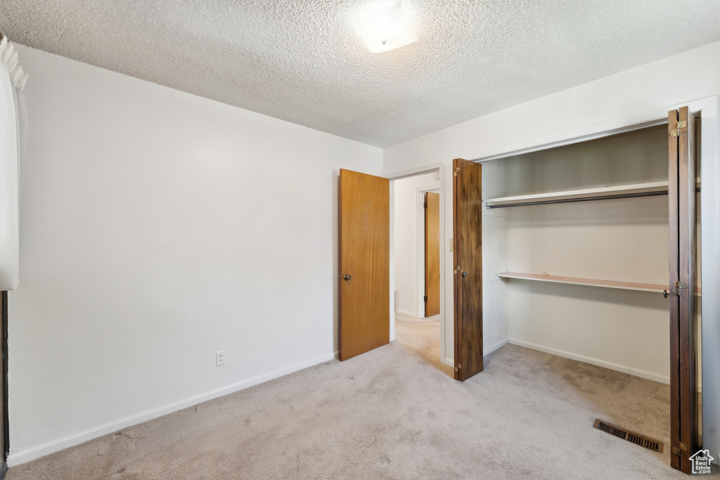 Unfurnished bedroom with carpet flooring, a textured ceiling, visible vents, and a closet
