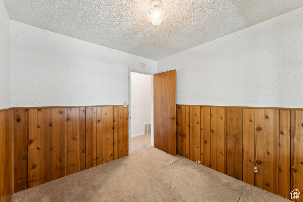 Carpeted empty room with visible vents, wainscoting, wooden walls, wallpapered walls, and a textured ceiling