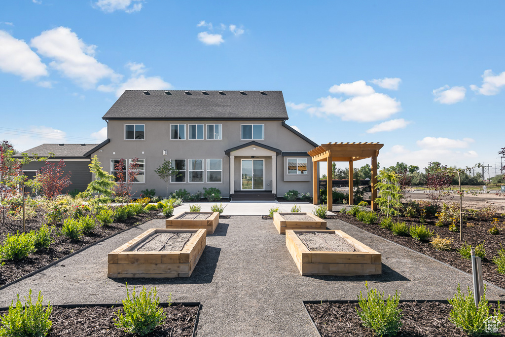 Rear view of property with a pergola, stucco siding, and a garden