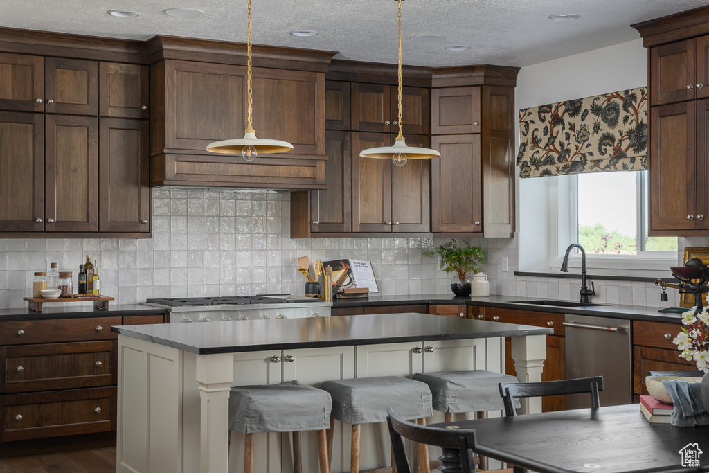 Kitchen with stainless steel dishwasher, dark countertops, a sink, backsplash, and hanging light fixtures