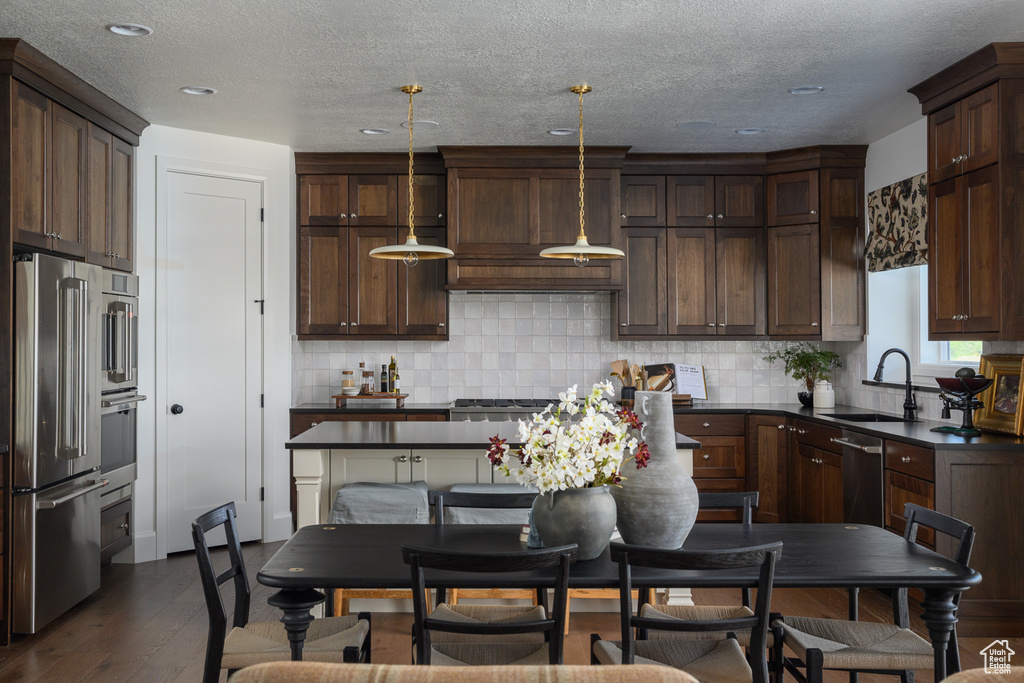 Kitchen with dark countertops, a sink, stainless steel appliances, tasteful backsplash, and dark wood-type flooring
