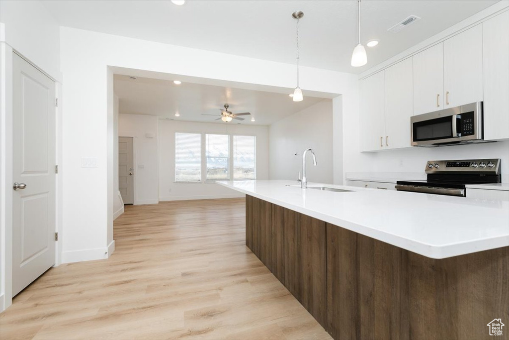 Kitchen with light wood-style floors, light countertops, white cabinets, a sink, and stainless steel appliances