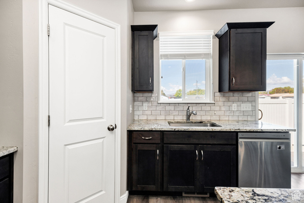 Kitchen with light stone countertops, a sink, dishwasher, wood finished floors, and tasteful backsplash