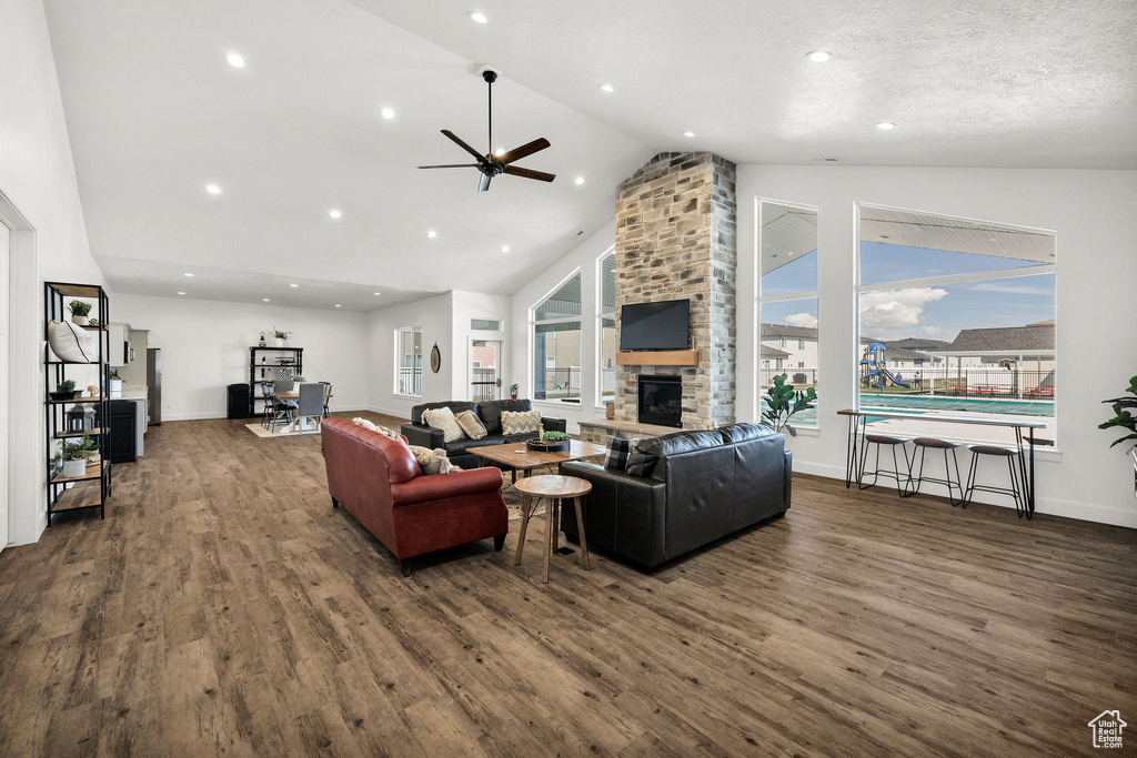 Living room with ceiling fan, a stone fireplace, high vaulted ceiling, baseboards, and dark wood-style floors
