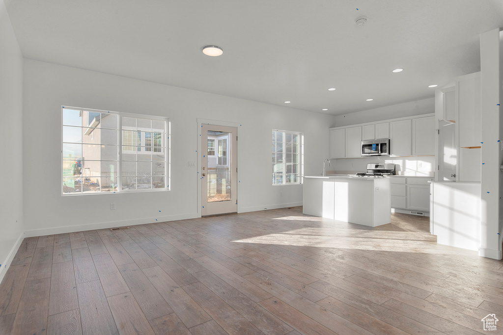 Unfurnished living room with a sink, baseboards, recessed lighting, and light wood-style flooring