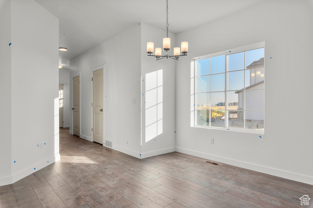 Unfurnished dining area with baseboards, visible vents, an inviting chandelier, and hardwood / wood-style flooring