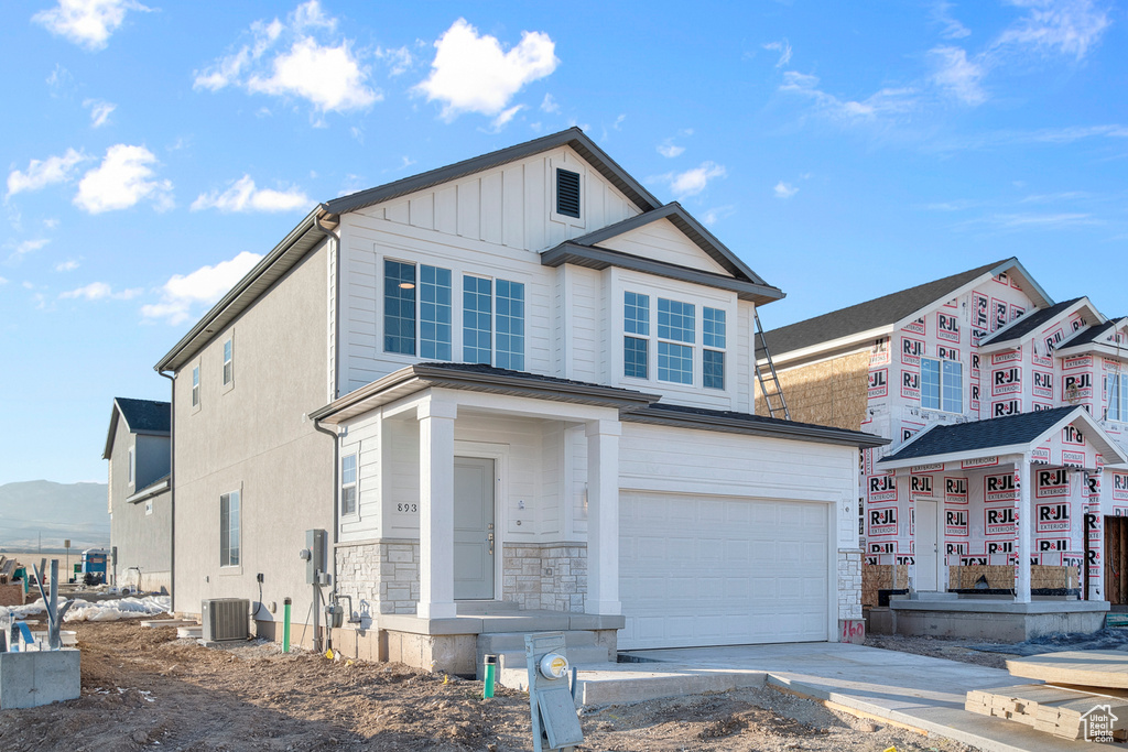 View of front of property featuring a garage, central air condition unit, driveway, and stone siding