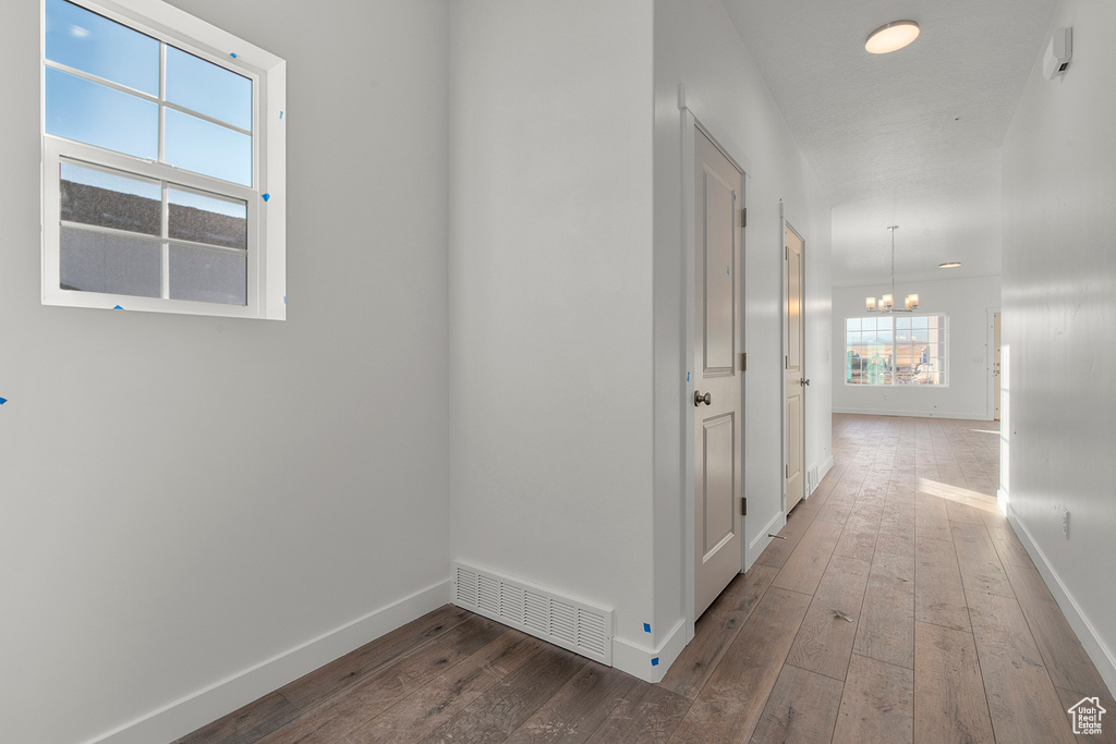 Hall with baseboards, a notable chandelier, hardwood / wood-style floors, and visible vents