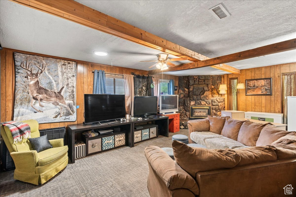 Carpeted living area with a ceiling fan, a textured ceiling, visible vents, beam ceiling, and wooden walls