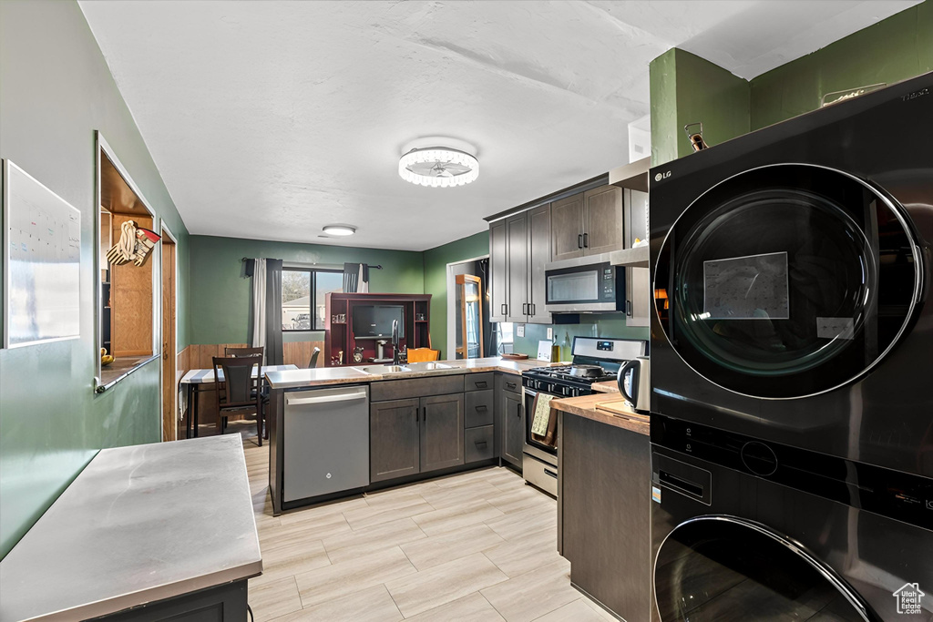 Kitchen with a sink, stacked washer / drying machine, stainless steel appliances, and a peninsula