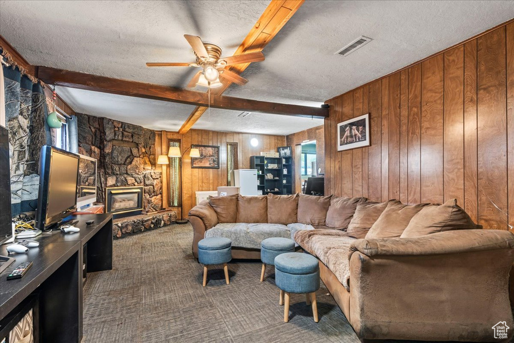 Living room with ceiling fan, a textured ceiling, carpet floors, beamed ceiling, and wooden walls