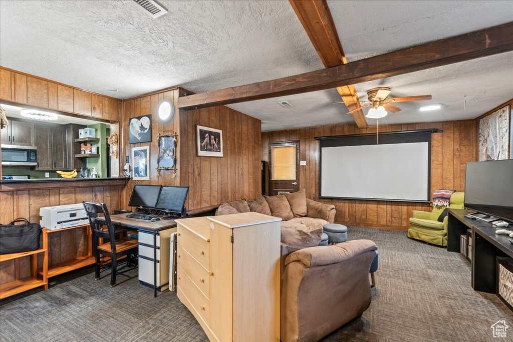 Home theater room with ceiling fan, visible vents, beamed ceiling, wooden walls, and carpet