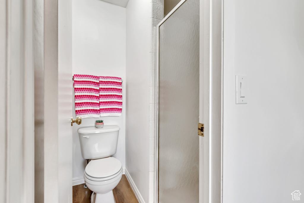 Full bathroom with toilet, baseboards, wood finished floors, and a stall shower