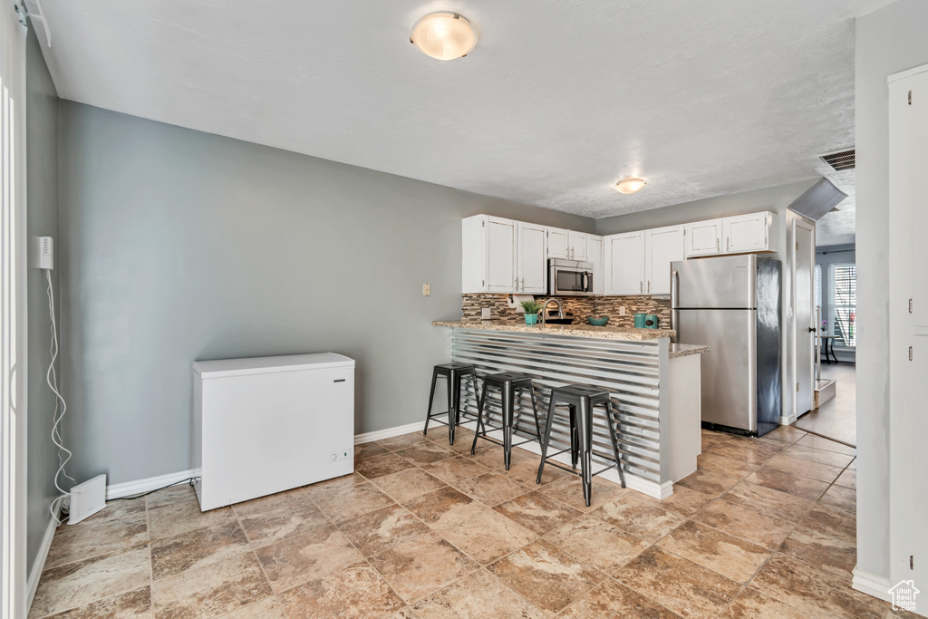 Kitchen with appliances with stainless steel finishes, baseboards, stone finish floor, and a peninsula