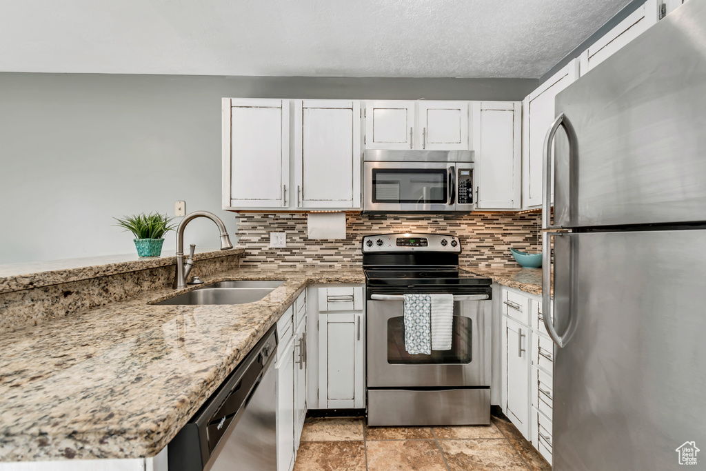 Kitchen with decorative backsplash, white cabinets, light stone counters, a sink, and appliances with stainless steel finishes
