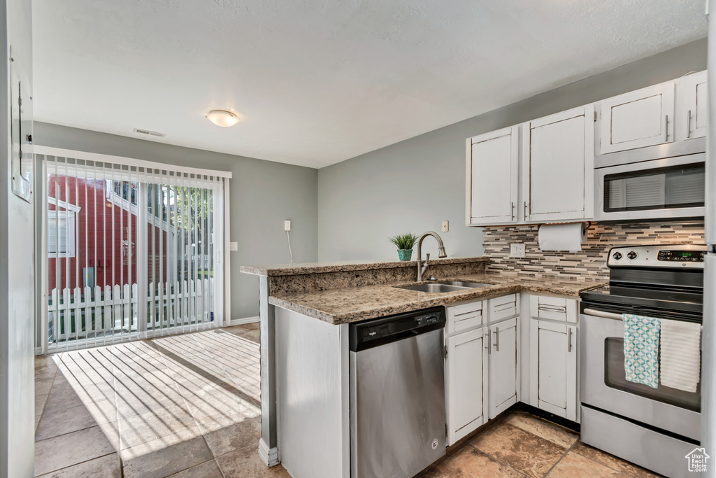 Kitchen with a sink, stainless steel appliances, white cabinetry, a peninsula, and decorative backsplash
