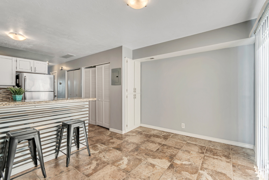 Kitchen with baseboards, white cabinets, freestanding refrigerator, and stone finish floor