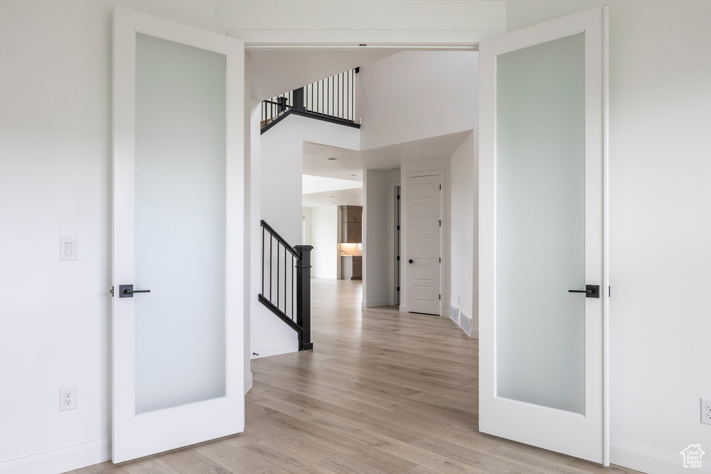 Corridor featuring stairway, baseboards, a high ceiling, and light wood-type flooring