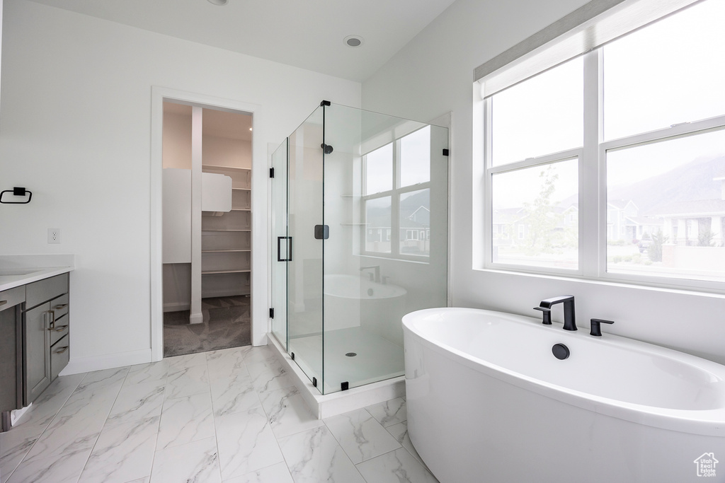 Full bathroom featuring marble finish floor, baseboards, a spacious closet, a soaking tub, and a stall shower