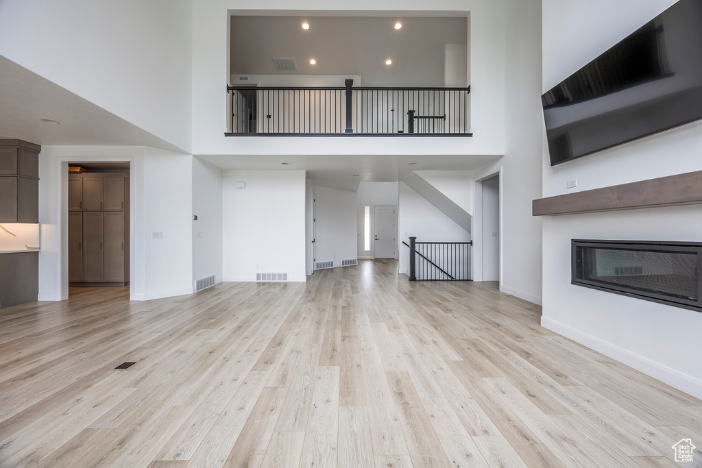 Unfurnished living room featuring visible vents, light wood finished floors, a glass covered fireplace, and a high ceiling