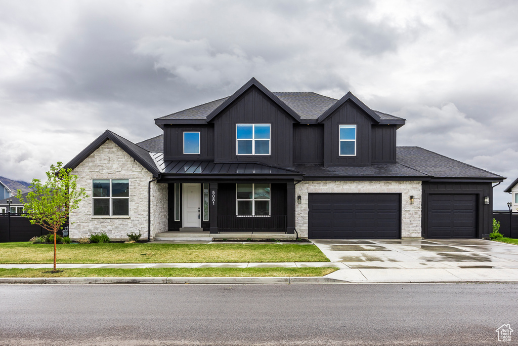 View of front of house with a front lawn, stone siding, a standing seam roof, a porch, and driveway