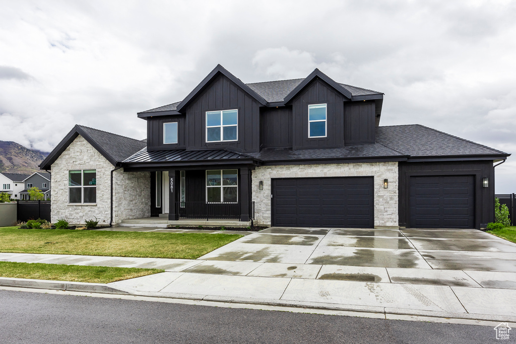 View of front of house with a shingled roof, a front lawn, concrete driveway, a standing seam roof, and covered porch