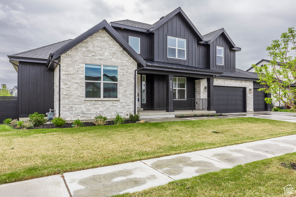 Craftsman-style house with covered porch, a front yard, stone siding, board and batten siding, and concrete driveway