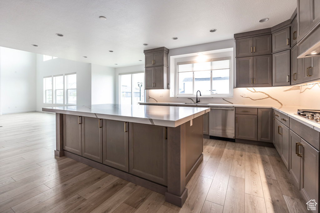 Kitchen featuring light wood-type flooring, appliances with stainless steel finishes, backsplash, and a center island